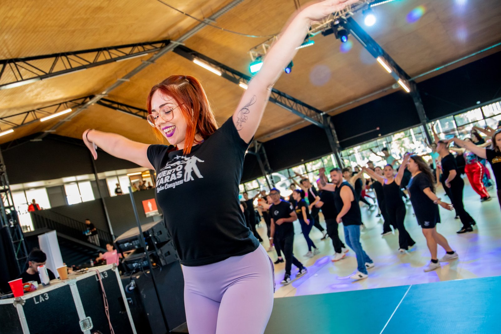Irene Palomares enseñando en un taller: sonríe con los brazos abiertos marcando el paso y, detrás, decenas de alumnas bailan