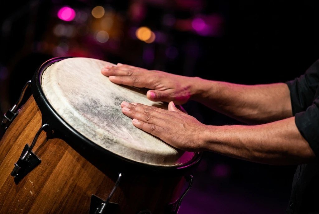 Manos de un percusionista golpeando el parche de una tumbadora de madera